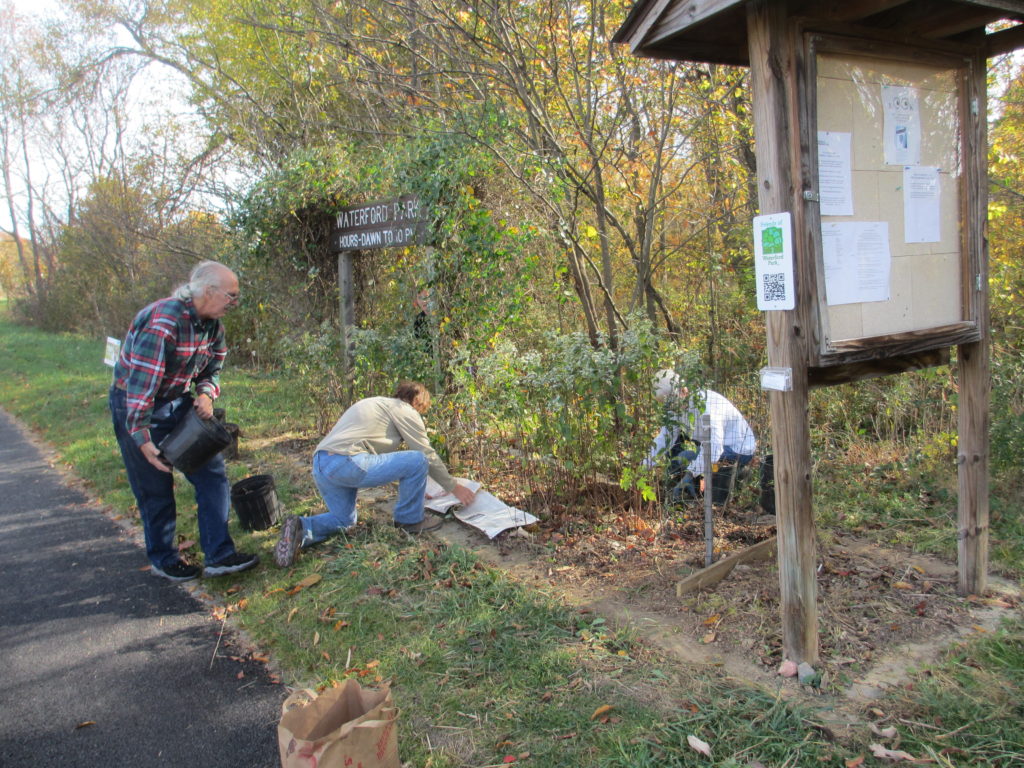 Kathy Soria, Fran Hostetler and Joe Ganley weeding and mulching the plants under the Waterford Park sign